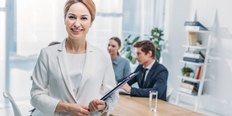 selective-focus-of-cheerful-recruiter-standing-with-clipboard-near-coworkers.jpg